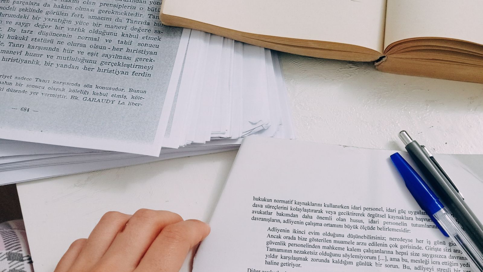 Hands reviewing open books and research notes at a study desk
