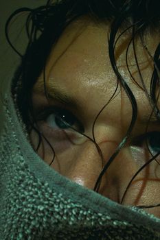 A moody close-up portrait of a person with wet hair wrapped in a towel, conveying a thoughtful expression.