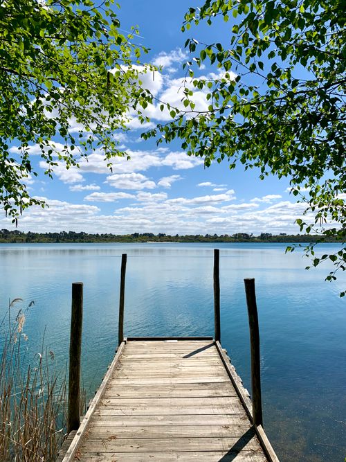 Free A serene wooden pier leading into a clear lake under a bright summer sky in Morcenx-la-Nouvelle, France. Stock Photo