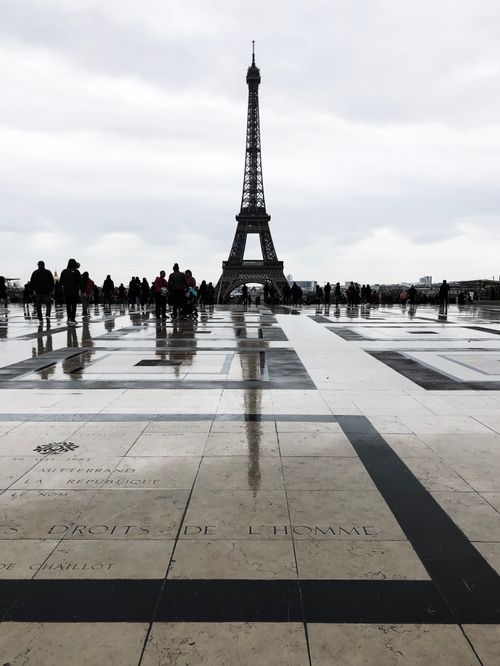 Free Tourists at Trocadéro with Eiffel Tower reflecting on wet ground under cloudy skies. Stock Photo