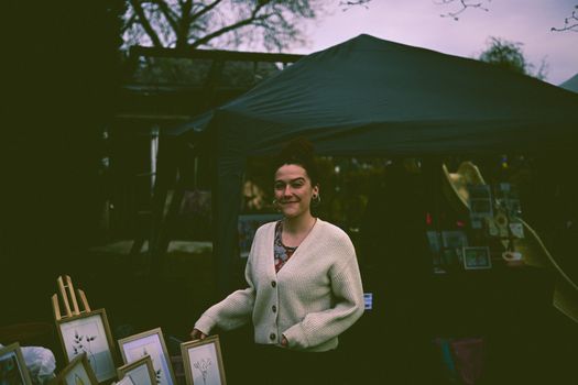 A woman smiles while selling handmade art prints at an outdoor market.