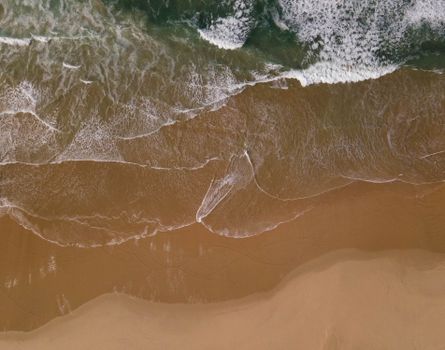 A captivating aerial shot of waves gently crashing onto a sandy beach, showcasing nature's beauty.