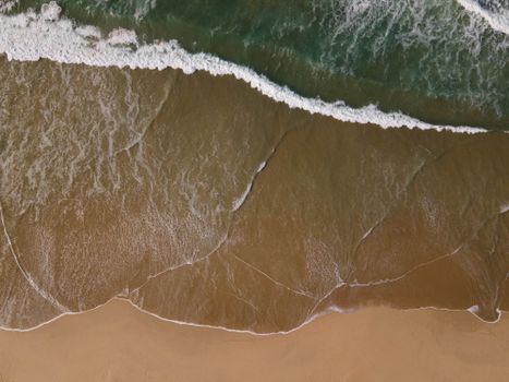 Stunning aerial view of ocean waves gently crashing onto a sandy beach shore.