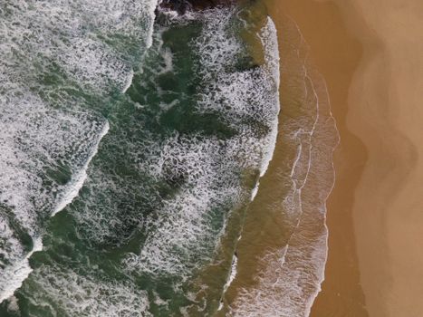 Aerial shot of ocean waves crashing onto a sandy beach, showcasing nature's beauty.