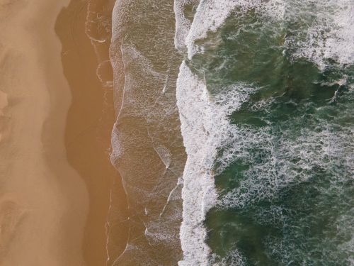 Free An aerial view of ocean waves meeting a sandy beach, showcasing natural beauty and coastal textures. Stock Photo