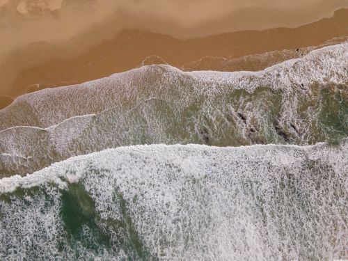 Free Stunning aerial view capturing the waves crashing on a sandy beach shore. Stock Photo