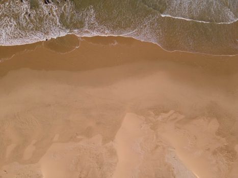 Top-down aerial view of waves crashing on sandy beach, capturing natural textures and patterns.