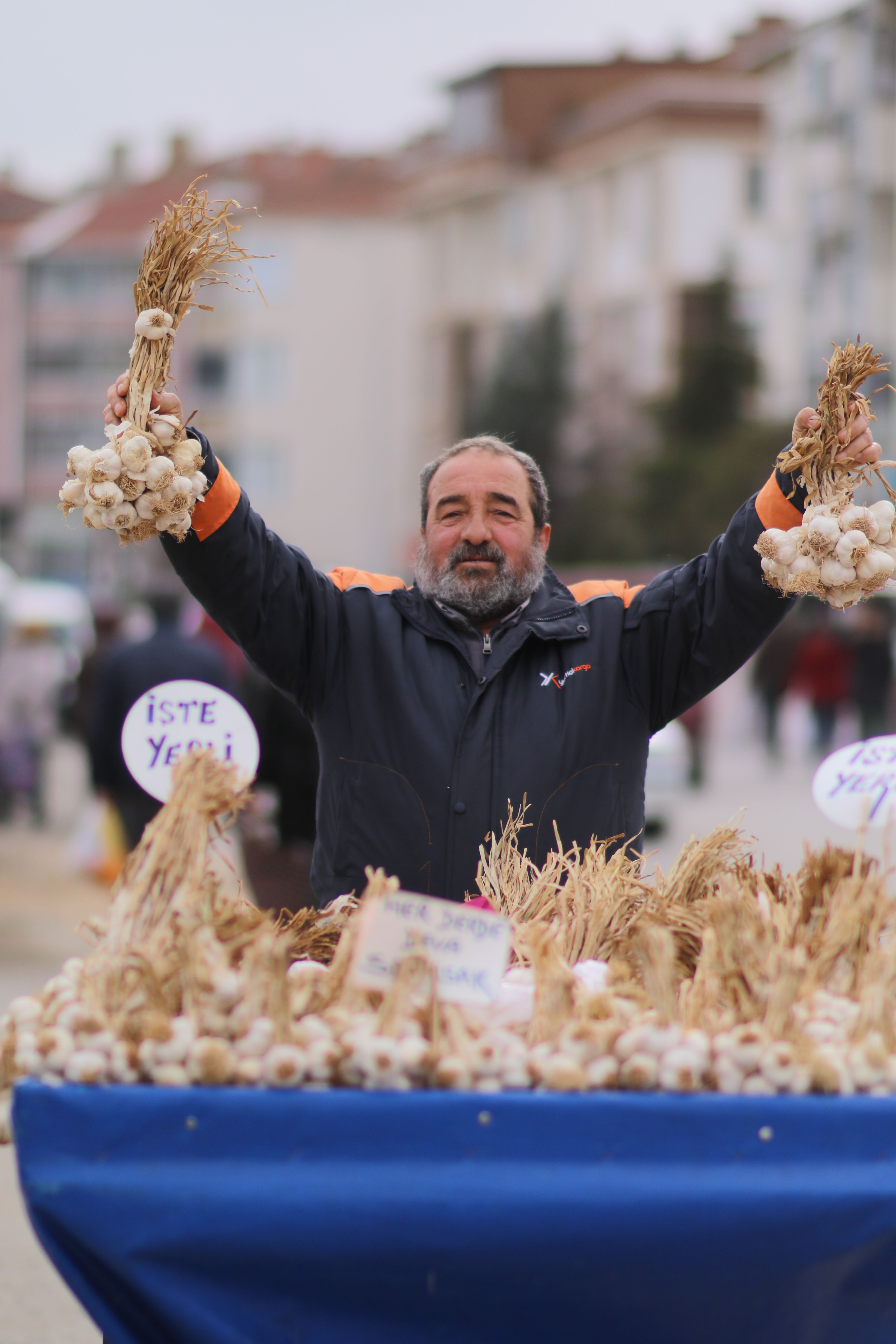 Man selling garlic at a bustling outdoor market, displaying vibrant local produce.