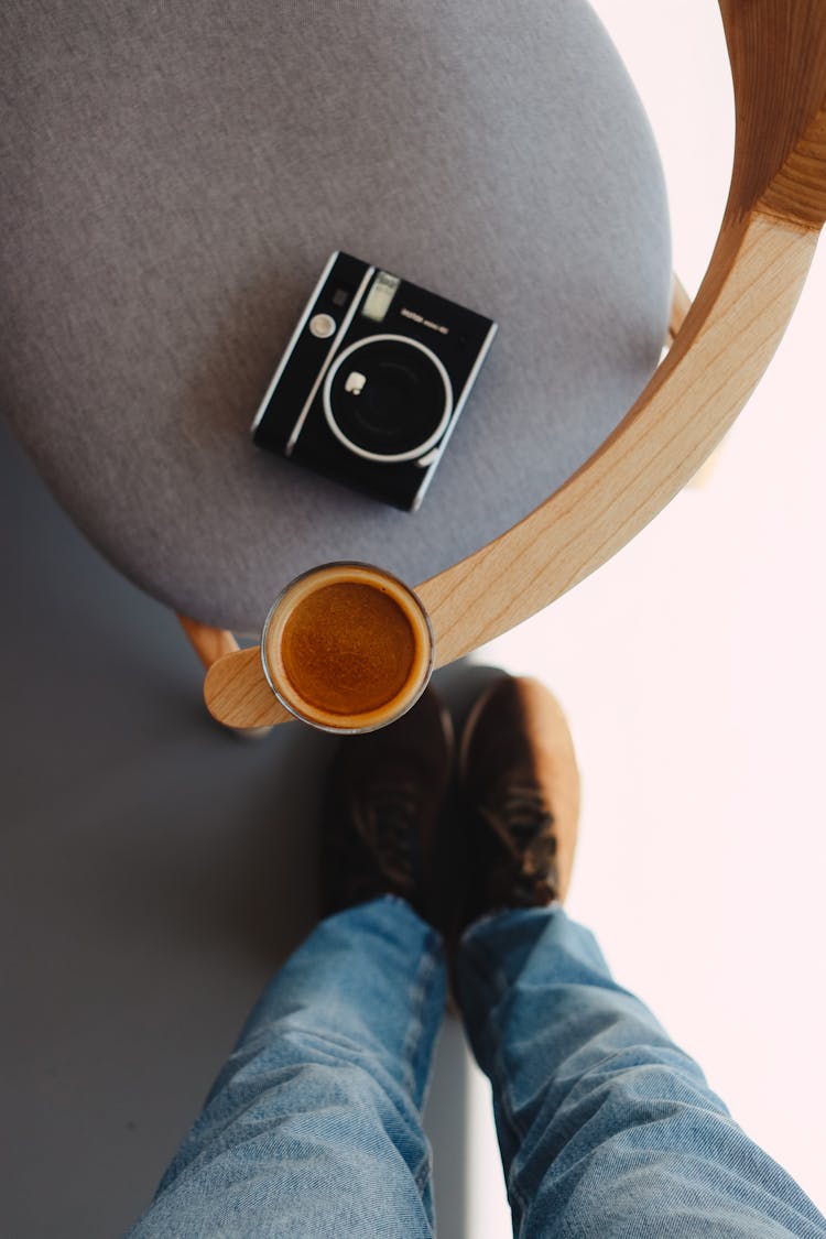 Legs Of Person Standing Over Chair With Coffee And Camera