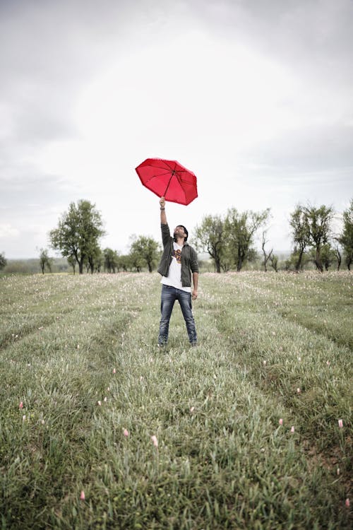 Man with a Red Umbrella Standing on a Meadow 