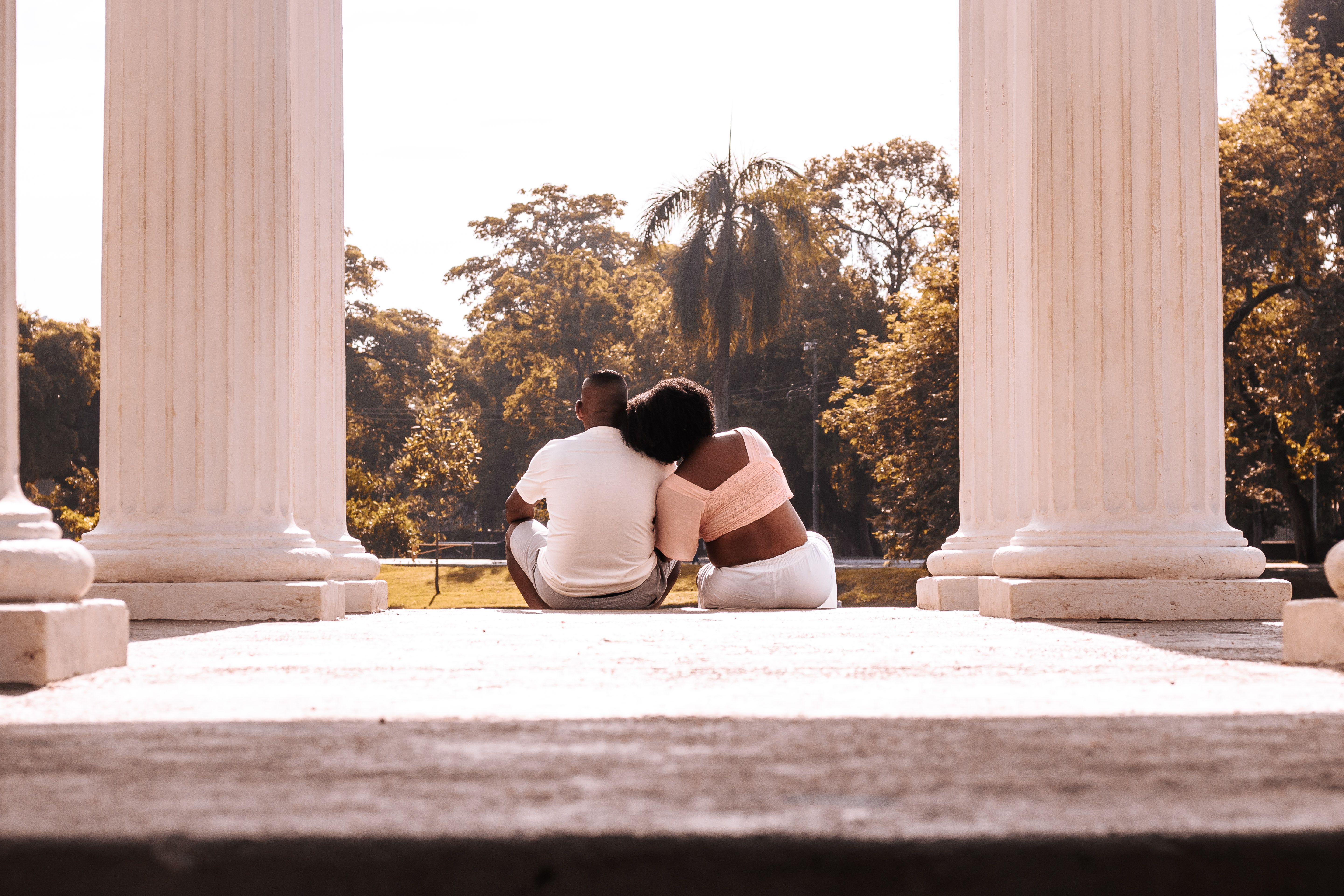 A couple sitting together outdoors between two classic columns, enjoying a sunny day.