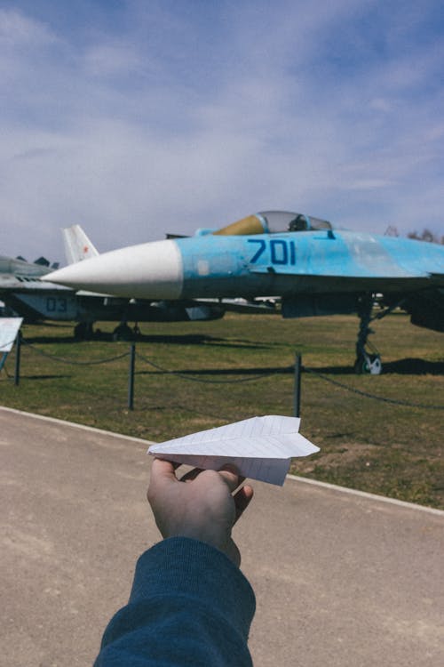 Man Holding a Paper Airplane on the Background of a Real Airplane in a Museum 