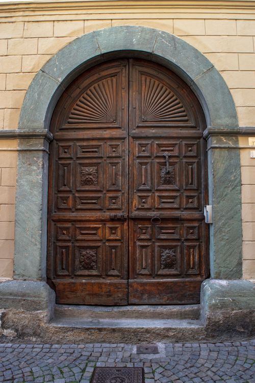 Free Vintage wooden door with intricate carvings set in a historic stone facade. Stock Photo