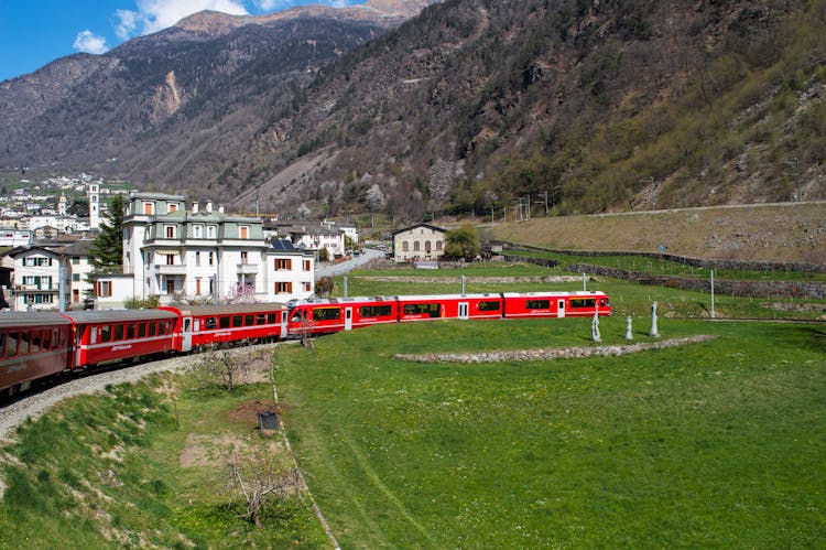 Swiss Red Train Bernina Express Passing By A Village In Mountains 