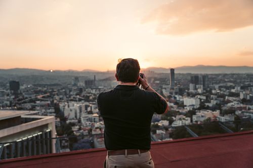 Free A man photographs Mexico City's skyline from a rooftop at sunset, capturing the urban landscape. Stock Photo