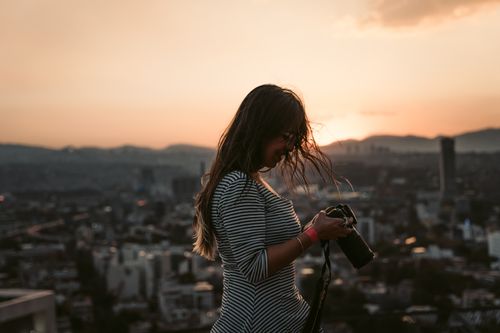 Free A woman photographs a stunning Mexico City skyline at sunset, creating a perfect urban panorama. Stock Photo