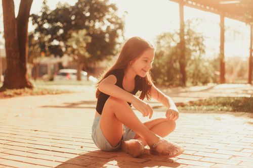 Free A happy child sitting and smiling on a sunlit sidewalk in the park. Stock Photo
