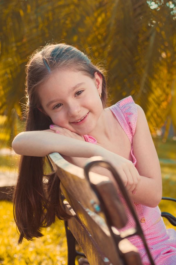 Smiling young girl in pink sitting on a park bench