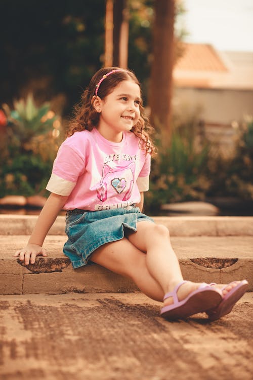 Little Girl in Pink T-Shirt and Denim Skirt Sitting on Pavement