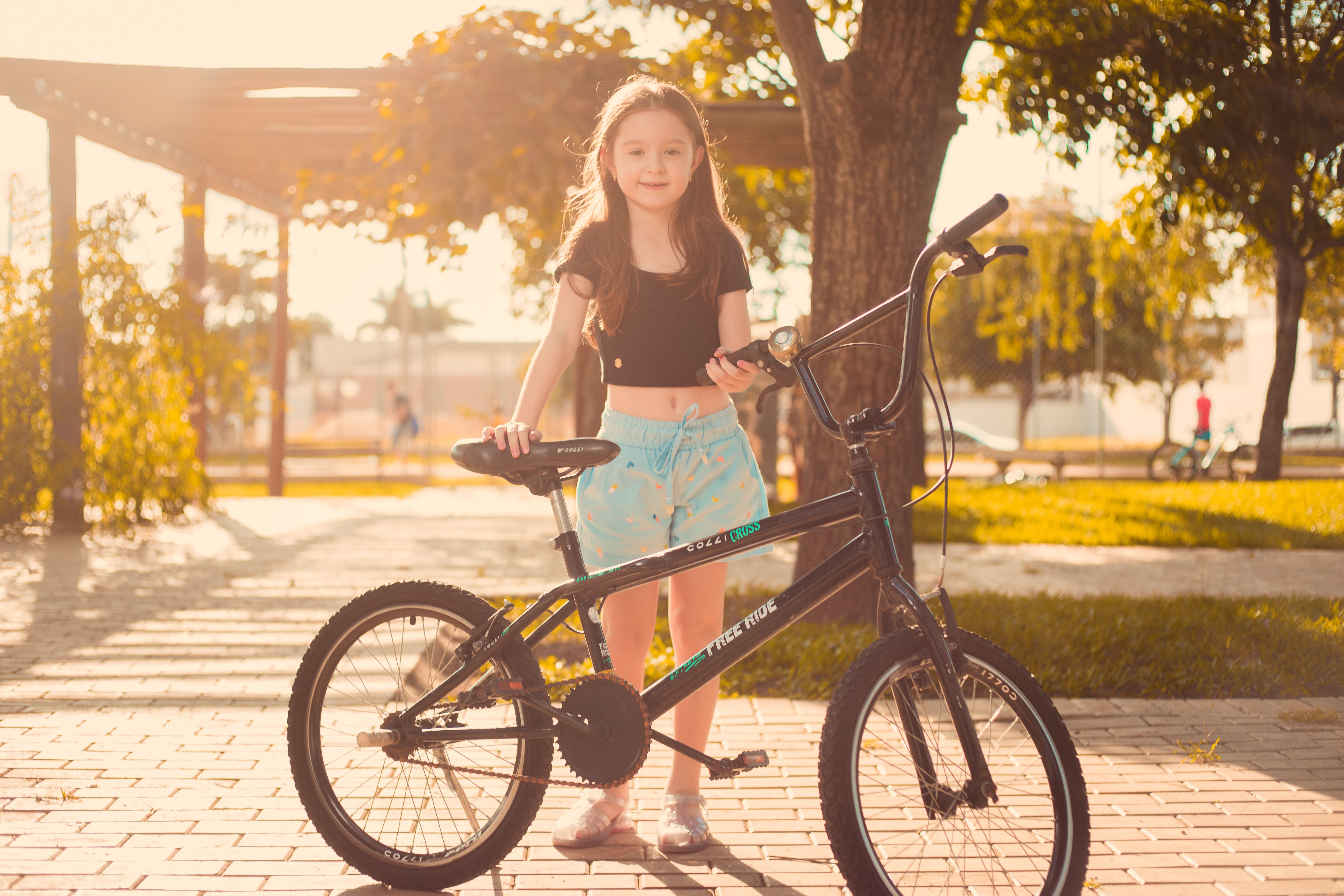 A smiling girl standing with her bike on a sunny day in a park.