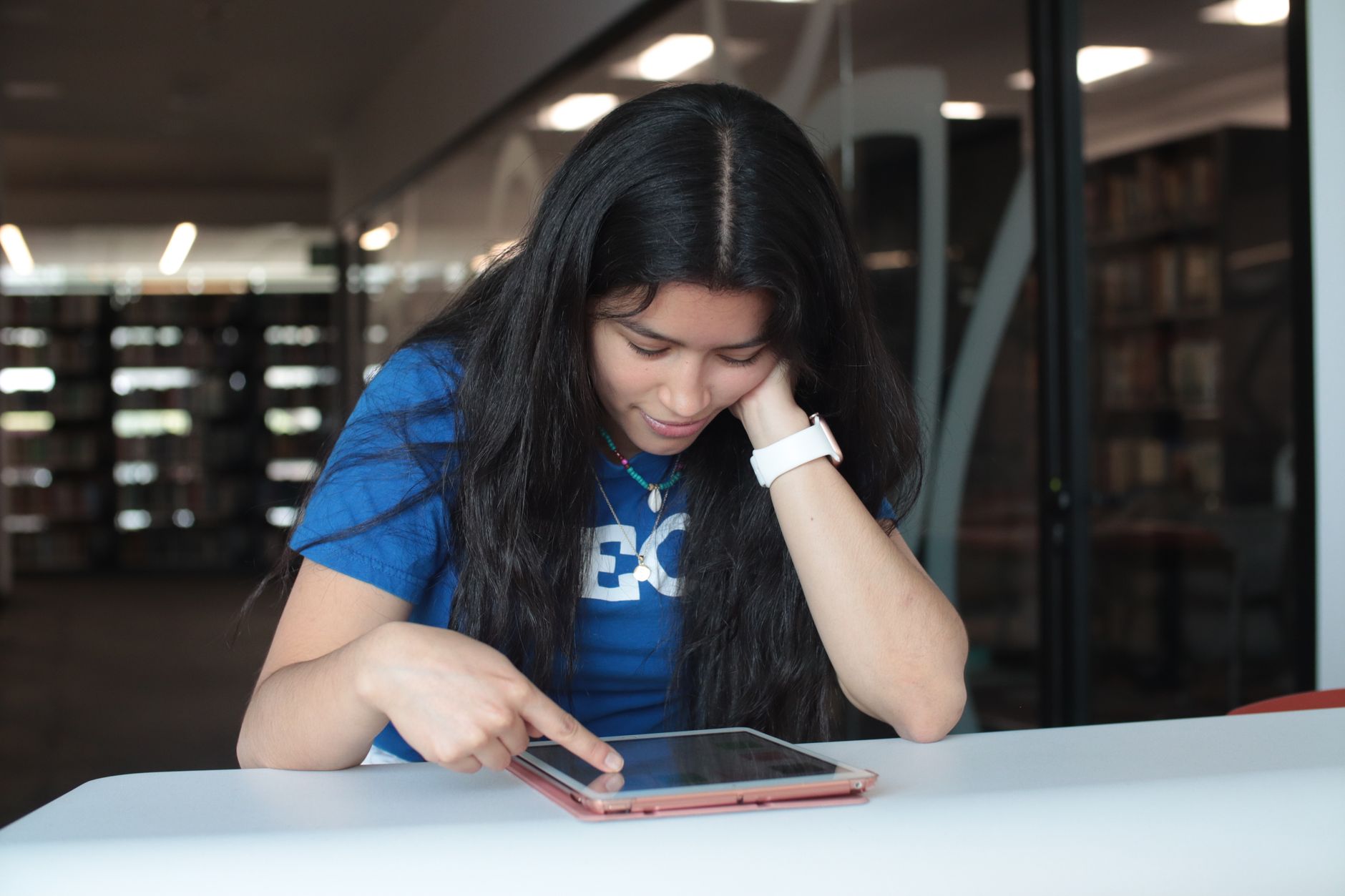 為何每個人都該具備數位素養?生活工作全面指南 A young woman in a blue t-shirt is using a tablet at a library table. Focused and engaged in her task.