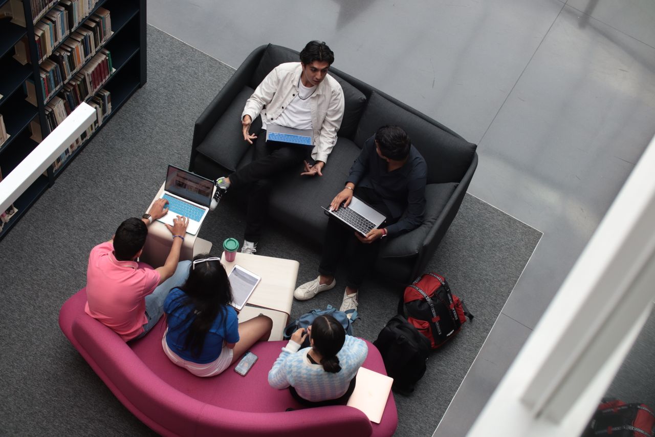 A group of diverse students using laptops and books in a library setting.