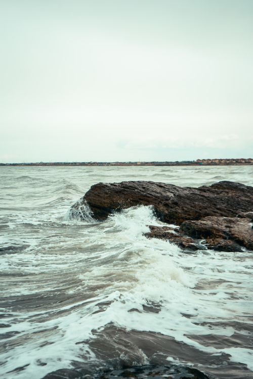 Free Dramatic waves crashing against rocks on a serene seashore on a cloudy day. Stock Photo