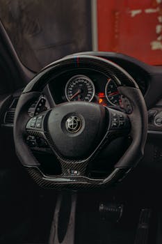 Close-up of a BMW steering wheel in a luxury car's cockpit, featuring carbon fiber design.