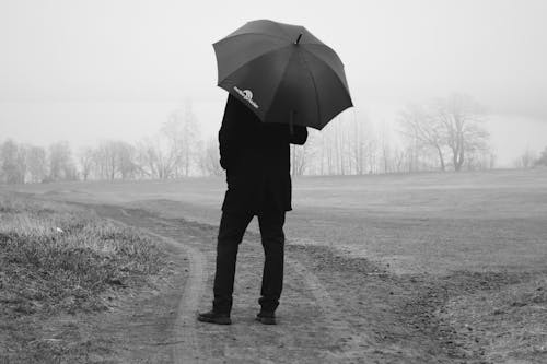 Back View of Man with Umbrella Standing on Dirt Road