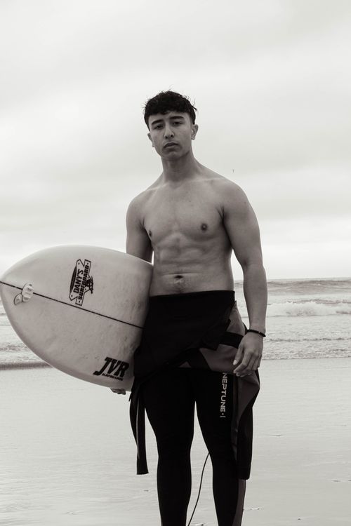 Free Black and white photo of a young male surfer holding a surfboard on the beach. Stock Photo