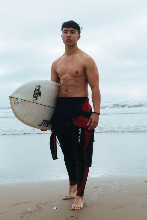 Free Muscular young man in wetsuit with surfboard on an ocean beach. Perfect for portraying outdoor activities and lifestyle. Stock Photo