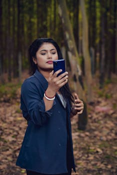 Stylish woman standing in a forest, using a smartphone while posing.