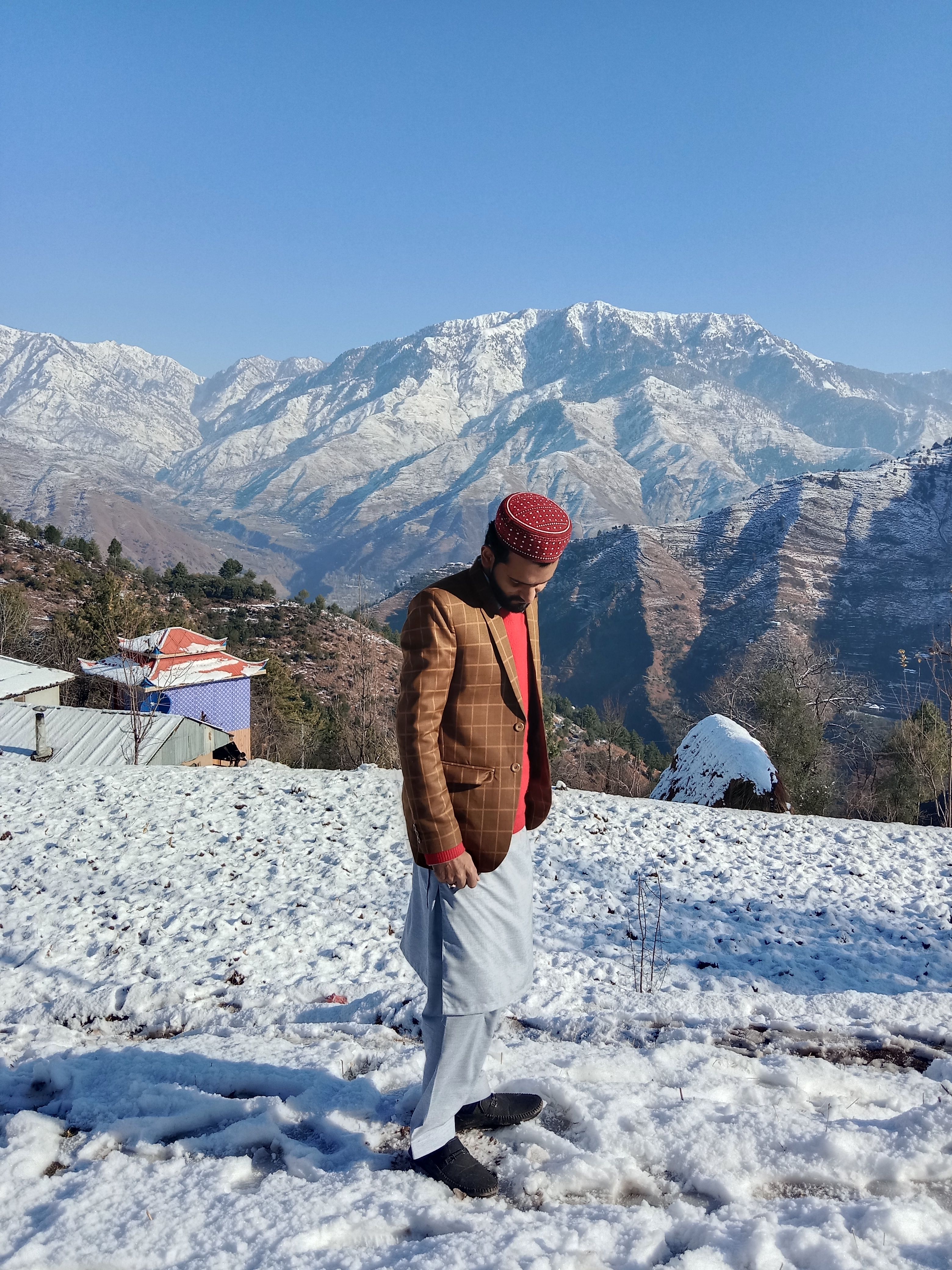Elegant man in traditional attire walking through snowy mountain landscape, capturing a serene winter moment.