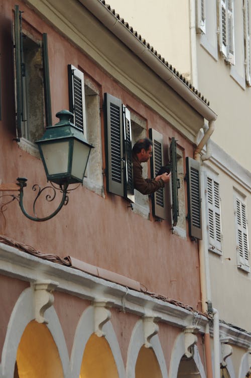 A Man Looking out the Window of a Traditional Building with Wooden Shutters 