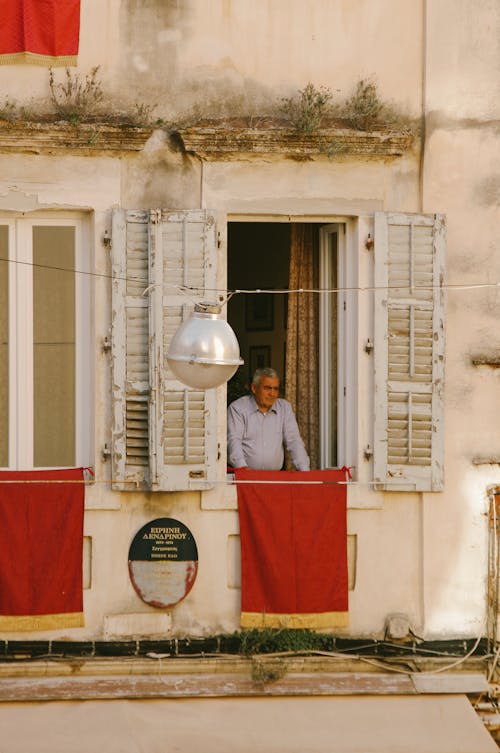 Free A Man Standing in the Window of a Traditional Building with Wooden Shutters  Stock Photo