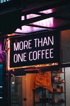 Neon sign reading 'More Than One Coffee' at an urban cafe, glowing at night.
