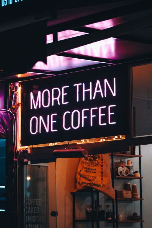 Free Neon sign reading 'More Than One Coffee' at an urban cafe, glowing at night. Stock Photo