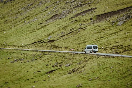 Free Aerial view of a van driving on a scenic road surrounded by lush green hillsides. Stock Photo