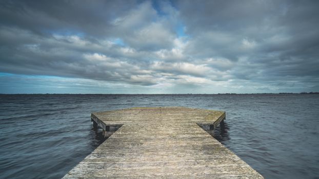 A serene wooden pier stretching into calm waters under a dramatic cloudy sky, capturing tranquility and nature's beauty.