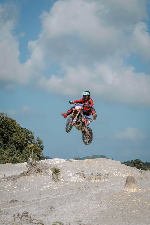 Free A skilled motocross rider performing a jump on a dirt track under a clear sky. Stock Photo