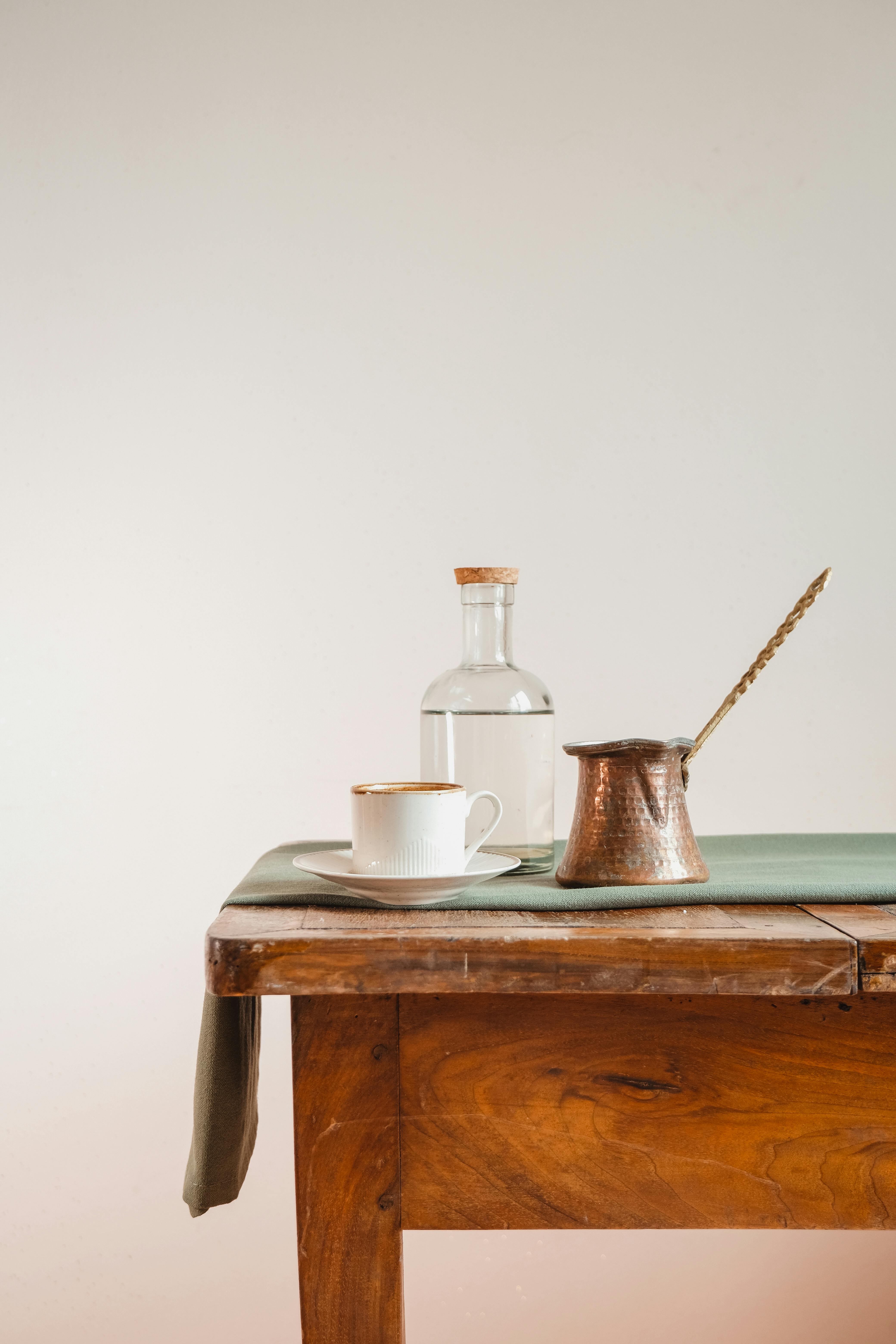 Elegant composition of a coffee setup featuring a copper pot, ceramic cup, and glass bottle on a wooden table.