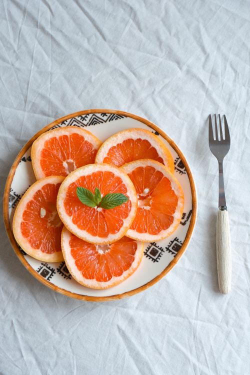 Free Vibrant orange slices arranged beautifully on a patterned plate with a fork beside them. Stock Photo