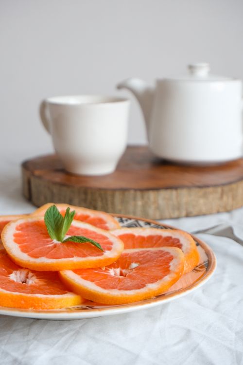 Free Vibrant grapefruit slices on a decorative plate with a teapot and teacup, perfect for a fresh breakfast setting. Stock Photo