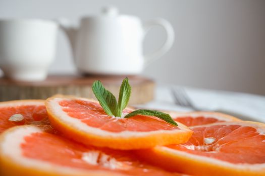 Close-up of juicy grapefruit slices with fresh mint leaves and a teapot in the background.