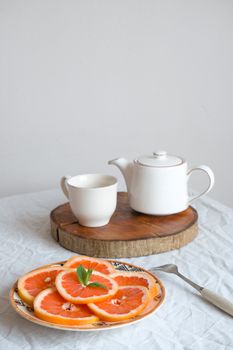 A refined table setting featuring a teapot, cup, and fresh orange slices on a white tablecloth.