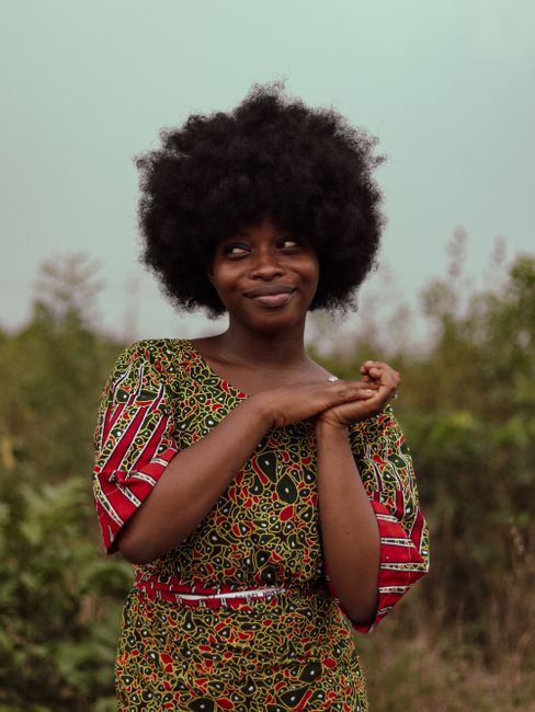 Portrait of a smiling woman in a colorful African print dress with a natural afro hairstyle.