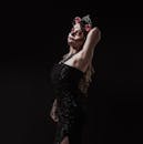 一位迷人的女人化着卡特里娜妆容，身着深色连衣裙，在黑色背景下摆出姿势