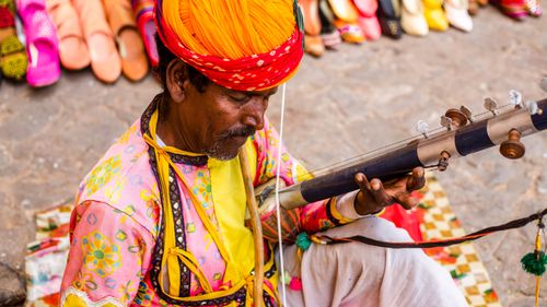 Free Colorful Rajasthani musician playing traditional instrument in vibrant street setting. Stock Photo