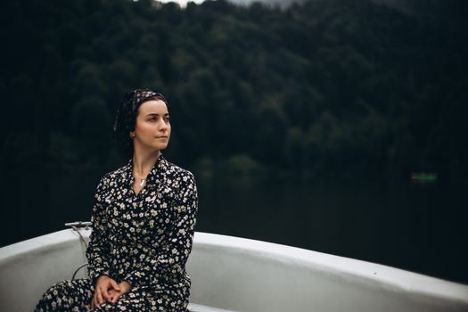 A woman in a floral dress sits calmly on a boat amidst lush Turkish forests.
