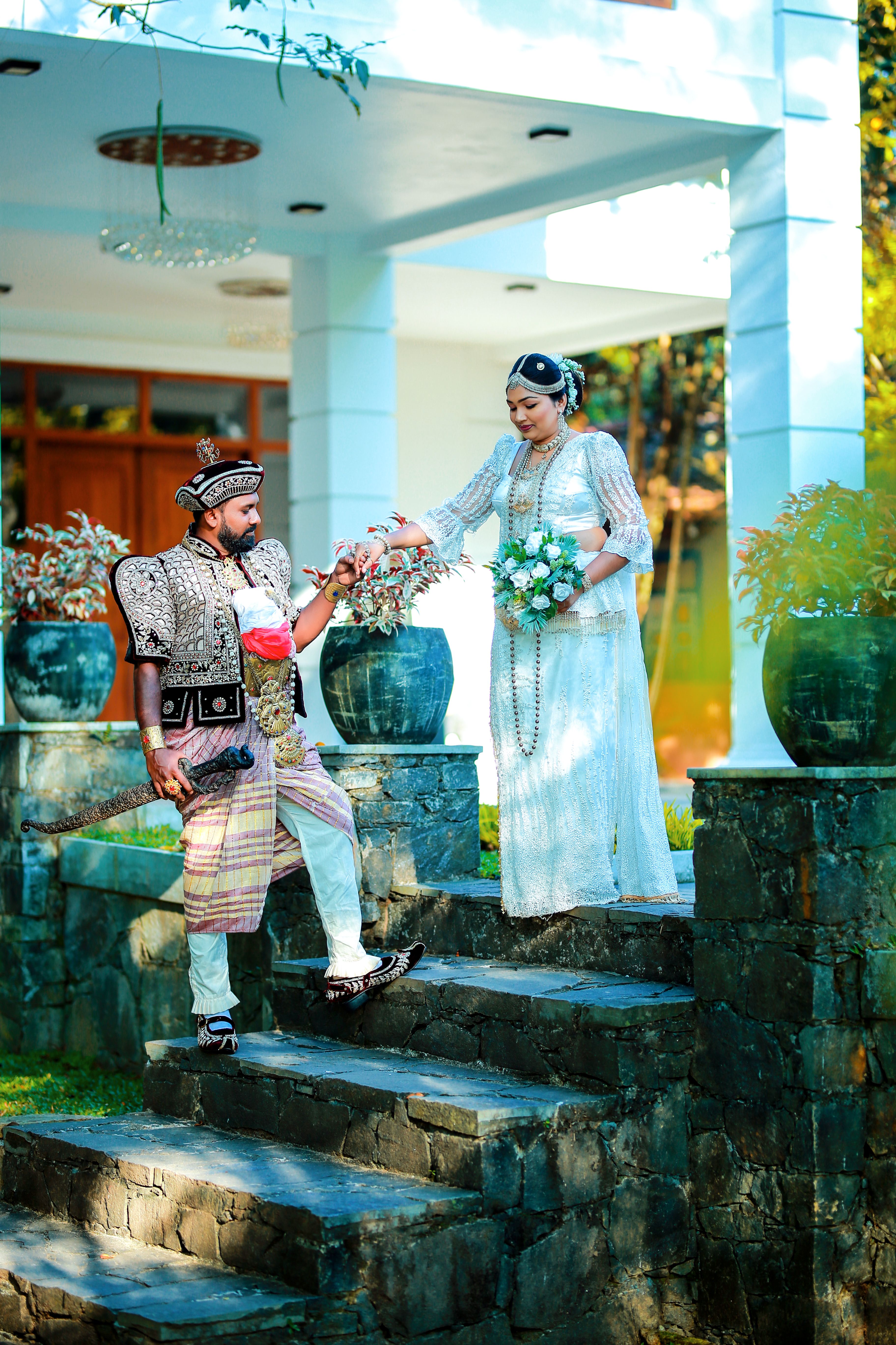 A couple in traditional attire exchanging floral gestures on stone steps outdoors.